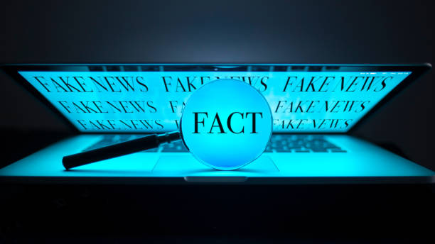 FAKE NEWS a magnifying glass on a laptop in the dark shows the word fact, in the background on the screen there are fake news speaking with forked tongue stock pictures, royalty-free photos & images