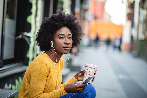 Portrait of African American woman outdoors using smart phone and listening podcast with headphones