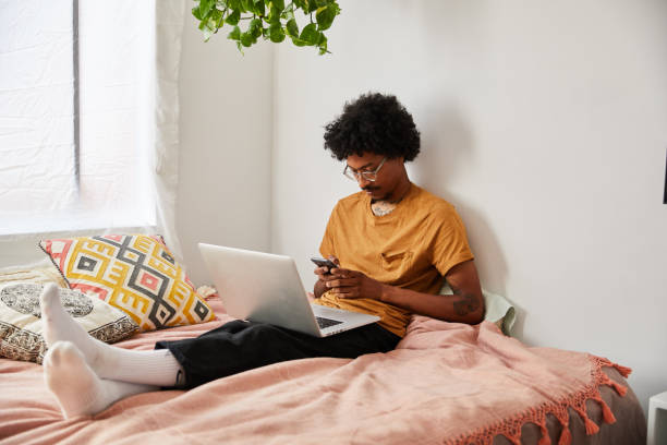 istock Young man using a cellphone and laptop while sitting on his bed 1270242982