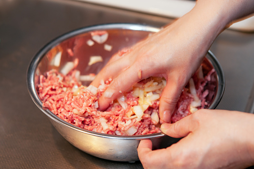 Woman's hands mixing minced flesh and other ingredients for cooking hamburgs in a bowl.