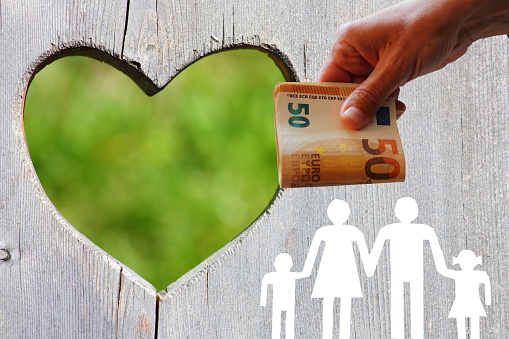 Family on wooden background with green heart and money in hand