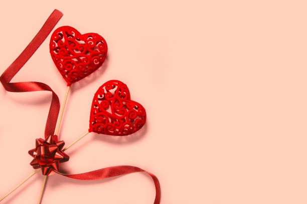 istock Abstract composition with two decorative hearts with red ribbon on pink paper background. 1270251715