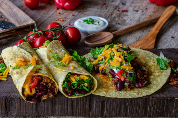 burritos on wooden background fresh and homemade burritos with minced meat and beans filling served on a wooden rustic board - mexican food - ready to eat burrito stock pictures, royalty-free photos & images