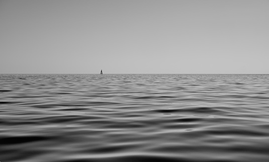 black and white seascape of calm sea with sails boat in the background - peace and relax concept