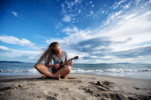 Teenage girl playing ukulele on beach on a beautiful summer day.\nNikon D850