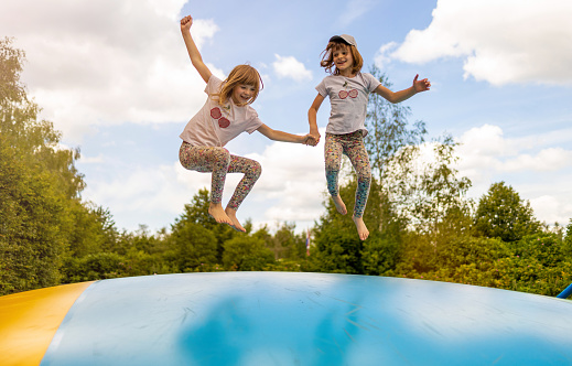 Little preschool girl jumping on trampoline. Happy funny toddler child having fun with outdoor activity in summer. Sports and exercises for children. Trampolin in ukrainian flagg colors.