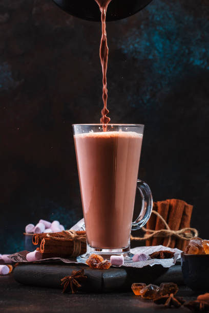 istock Pouring winter hot chocolate cocoa drink into tall glass with ispices on black table. Dark blue background. Copy space 1270259169