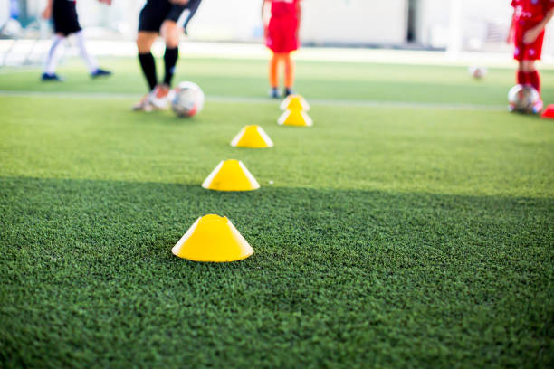 istock selective focus to yellow cone marker is soccer training equipment on green artificial turf with blurry kid players training background. 1270261898