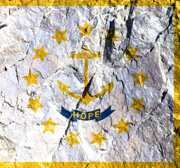 Flag of American state of Rhode Island is painted on mountain wall in circle of thirteen gold five-pointed stars. In center there gold anchor, under which is blue ribbon with gold inscription "Hope"