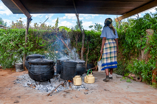 African woman, cooking in few Big pots outdoors in the village, African kitchen in the backyard