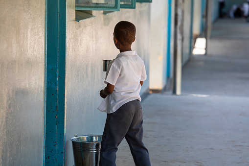 Thirsty African child at school drinking water from a bucket