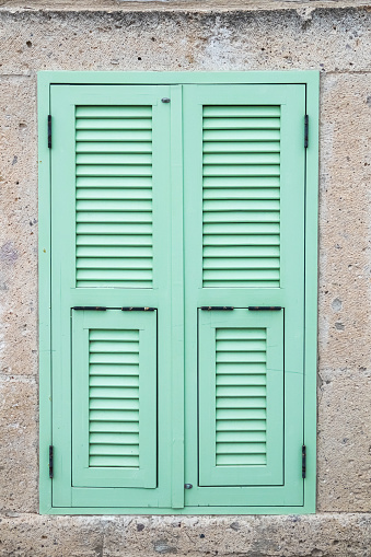 Turquoise window shutter on stone wall.