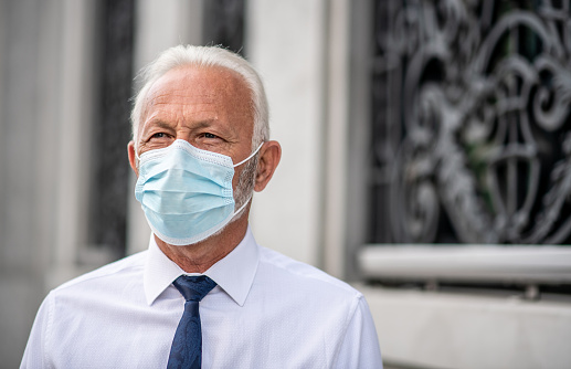 Mature businessman in suit thinking and wearing mask against concrete wall