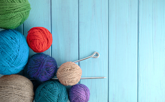 Balls of yarn in different colors with knitting needles on a background of blue wood texture.