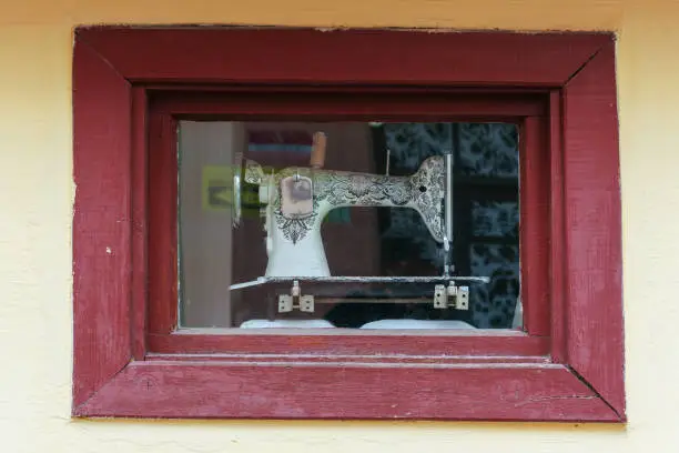 vintage old sewing machine behind window in wooden frame of antique sew salon front view