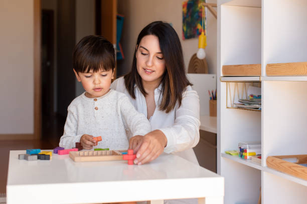 istock Kid playing with a game wood puzzle and mother or teacher help. Homeshooling. Learning Community. Montessori School 1270275434