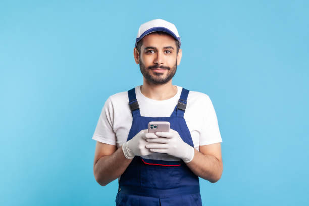 istock Handyman in overalls and gloves holding mobile phone, using cellphone messenger to accept online order 1270275541