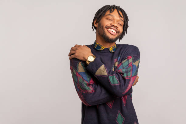 satisfied pleased african man in casual sweatshirt with dreadlocks hugging himself, egoistically comforting and relaxing, self esteem - urgency body care young adult people imagens e fotografias de stock