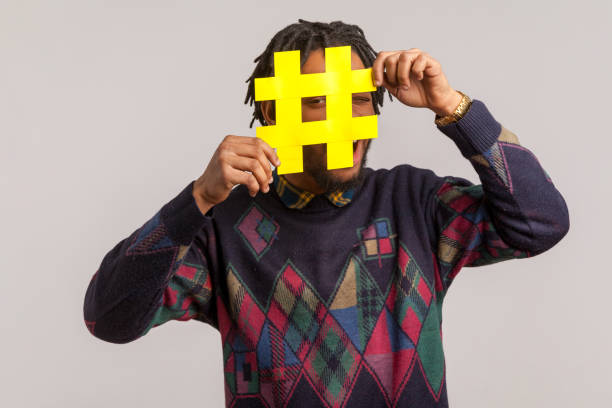 verspielte glückliche afrikanische kerl mit dreadlocks in trendigen sweatshirt versteckt gesicht hinter hashtag-symbol, beliebte blogger empfiehlt, tag zu folgen, kommentare - popular culture fotos stock-fotos und bilder