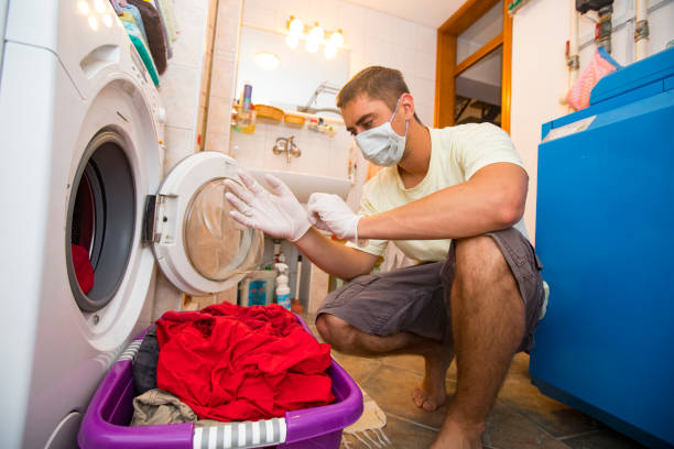 hombre adulto joven que lleva guantes de protección y máscara facial al poner ropa sucia en la lavadora - contamination meter fotografías e imágenes de stock