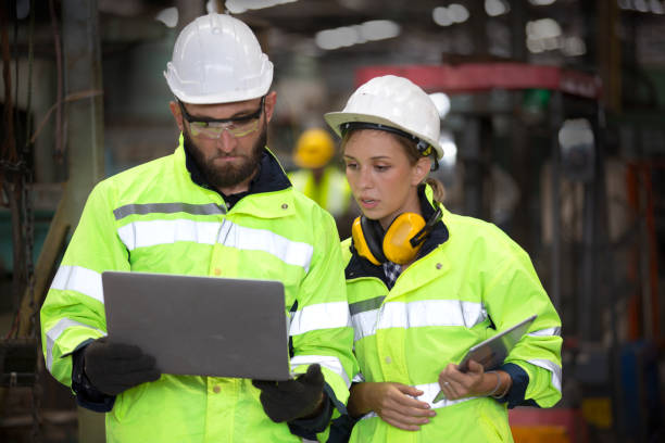 istock Two Industrial Engineers Talk with Factory Worker while Using Laptop. They Work at the Heavy Industry Manufacturing Facility. 1270276270