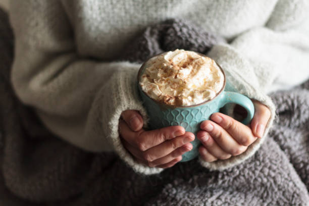 Woman with blanket warming her hands in mug of hot drink with whipped cream Woman with blanket warming her hands in mug of hot drink with whipped cream hot chocolate photos stock pictures, royalty-free photos & images