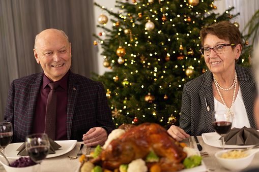 happy smiling senior couple sitting on christmas dinner table at home in austria with roasted turkey and decorated christmas tree