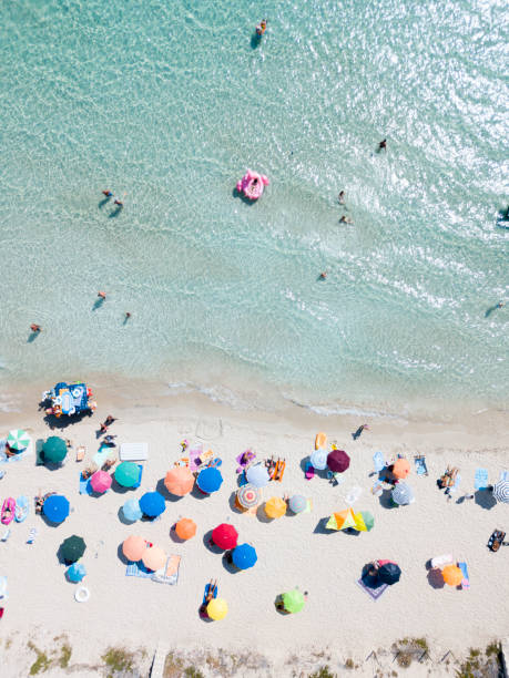 puglia, italia - 06 settembre 2018: vista aerea donna in bikini sdraiata su fenicottero rosa in mare azzurro, nuoto, bagno di sole, persone si rilassano sui lettini da spiaggia sotto gli ombrelloni, punta prosciutto. vacanze estive - umbrella beach sex symbol white foto e immagini stock