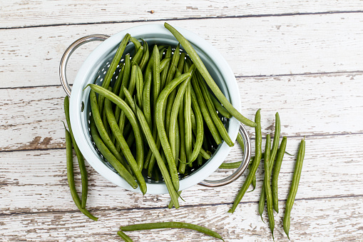 colander filled with French green beans sitting on a weathered table