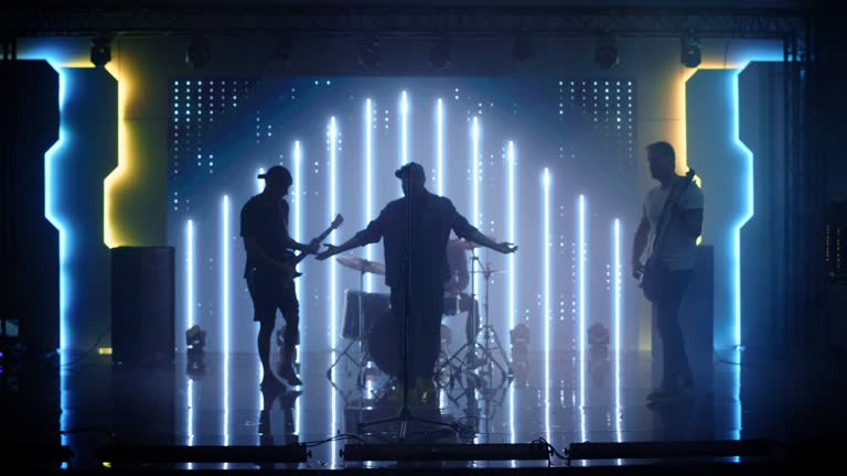 Four Man Rock Band with Lead Singer, Guitarists, Bassist and Drummer Performing at a Concert in a Night Club. Live Music Party in Front of Bright Colorful Strobing Lights on Stage.