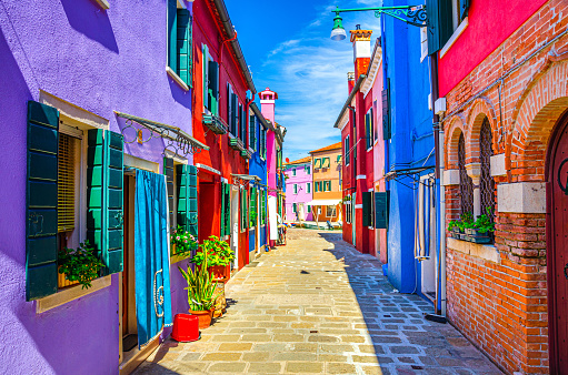 Burano island narrow cobblestone street between colorful houses buildings with multicolored bright walls, blue sky sunny summer day, Venice Province, Veneto Region, Northern Italy. Burano postcard