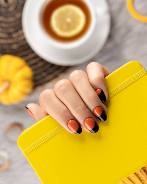 Manicured woman's hand holding yellow notepad on gray background. Manicured woman's hand holding yellow notepad on gray background. Trendy autumn halloween orange nail design. fall nail art stock pictures, royalty-free photos & images