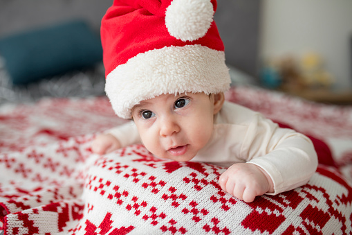 Portrait of newborn baby in Santa hat , lying on her tummy on a Christmas blanket in bed