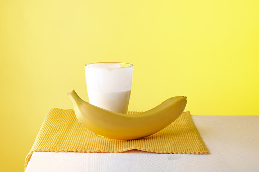 a glass with a dairy product and a banana on a yellow cloth napkin. healthy breakfast, harmonious colors