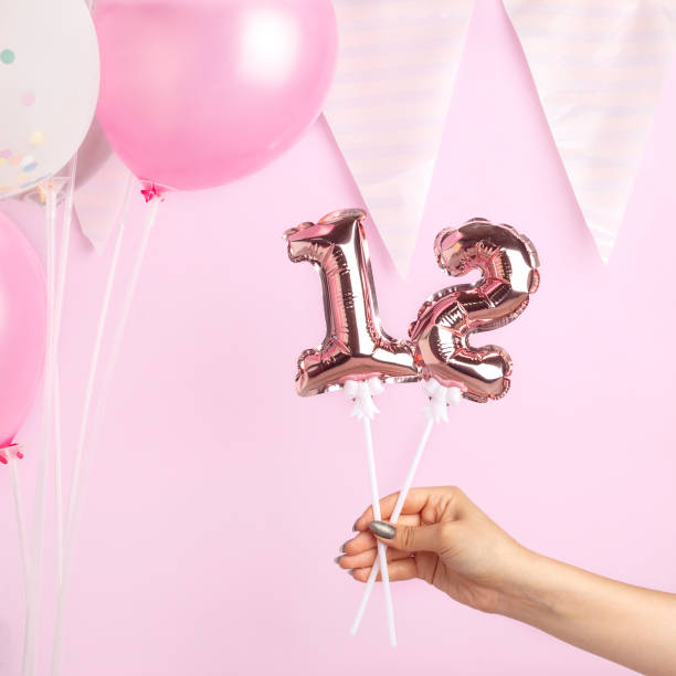 decoration for birthday party. female hand holding golden balloon in form of 12 number on pink background. - circa 12th century imagens e fotografias de stock