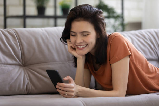 istock Smiling girl lying on couch texting on cell 1270295066