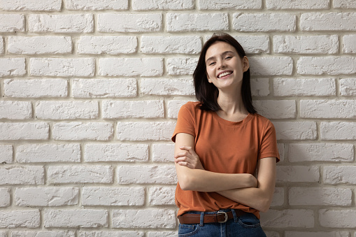 Portrait of happy millennial Caucasian girl teenager in casual clothes wear stand posing isolated on white brick wall, smiling young woman renter or tenant relocate move to own new home or apartment