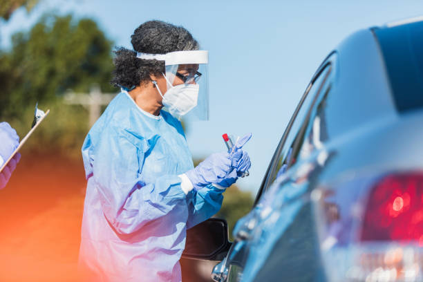 Female healthcare worker explains COVID test to patient A mature female healthcare professional explains the testing procedure to a patient at a drive through COVID-19 testing site. The healthcare professional is holding a COVID test kit. frontline worker mask stock pictures, royalty-free photos & images