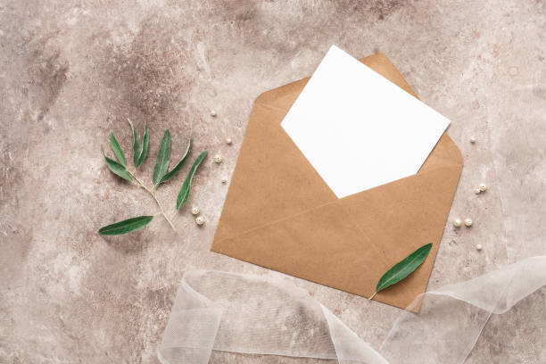 istock Wedding invitation template. Blank white card in a craft envelope, ribbon, olive branch and pearls. Beige grunge background. Top view, flat lay. 1270296331