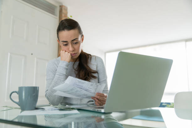 Woman paying her utility bills online and looking worried Woman paying her utility bills online and looking worried while staying at home during the pandemic - home finances concepts struggle stock pictures, royalty-free photos & images