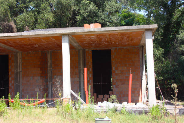 house under construction with exposed red bricks, concrete and supporting columns in architecture in a green pine forest of trees in tuscany