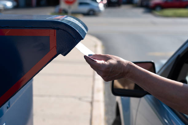 A woman is safely and contactlessly mailing in her application for ballot for the 2020 election Palatine, IL/USA - 08-27-2020:  Safely mailing an application for ballot for 2020 election at a  drive-up mailbox at the US Post Office united states postal service photos stock pictures, royalty-free photos & images