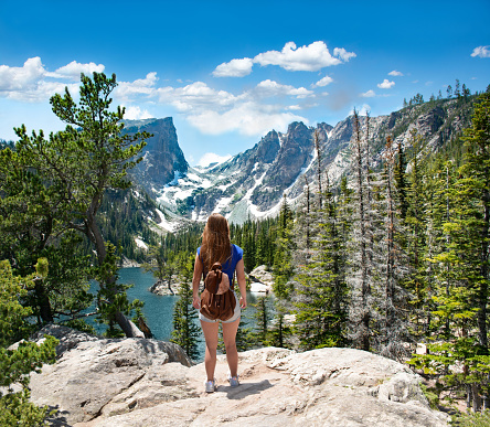 Girl enjoying  beautiful scenery on hiking trip. Early summer landscape with lake  and snow covered mountains.  Dream Lake, Rocky Mountains National Park, Colorado, USA.