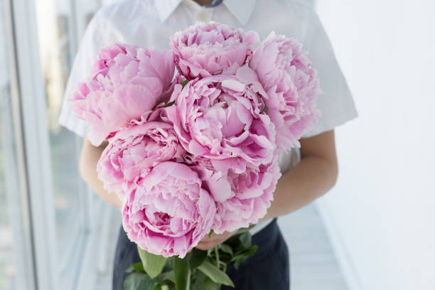 Photo of boy in white shirt hold big gentle bouquet of pink peony.