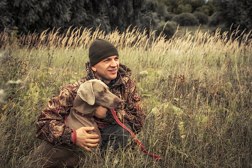 Hombre cazador con perro de caza Weimaraner en hierba alta en campo rural durante la temporada de caza photo