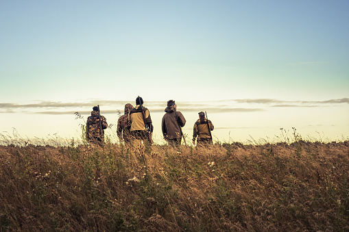 Los cazadores siluetas contra el cielo que atraviesan el campo rural hacia el horizonte durante la temporada de caza photo