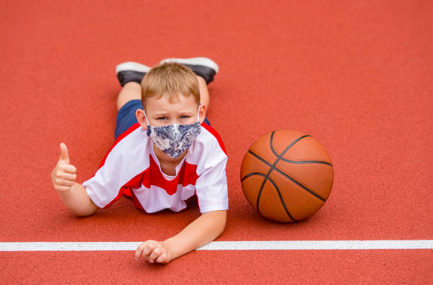 School kid with mask and basketball ball in a physical education lesson. Safe back to school during pandemic concept. Social distancing to fight COVID-19 School kid with mask and basketball ball in a physical education lesson. Safe back to school during pandemic concept. Social distancing to fight COVID-19 face guard sport photos stock pictures, royalty-free photos & images