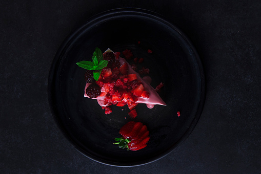 Slice of dessert with melted ruby red chocolate and strawberries on dark background