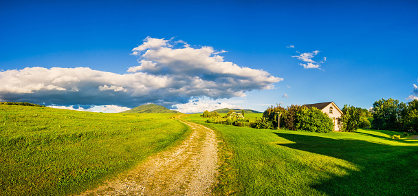 An unpaved road winds through a green pasture as it heads towards Burke Mountain in East Burke,  Vermont.