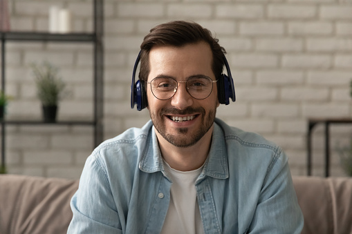Close up headshot portrait of smiling man in headphones glasses have webcam conference at home office, profile picture of happy male in earphones speak talk on video call, virtual event concept